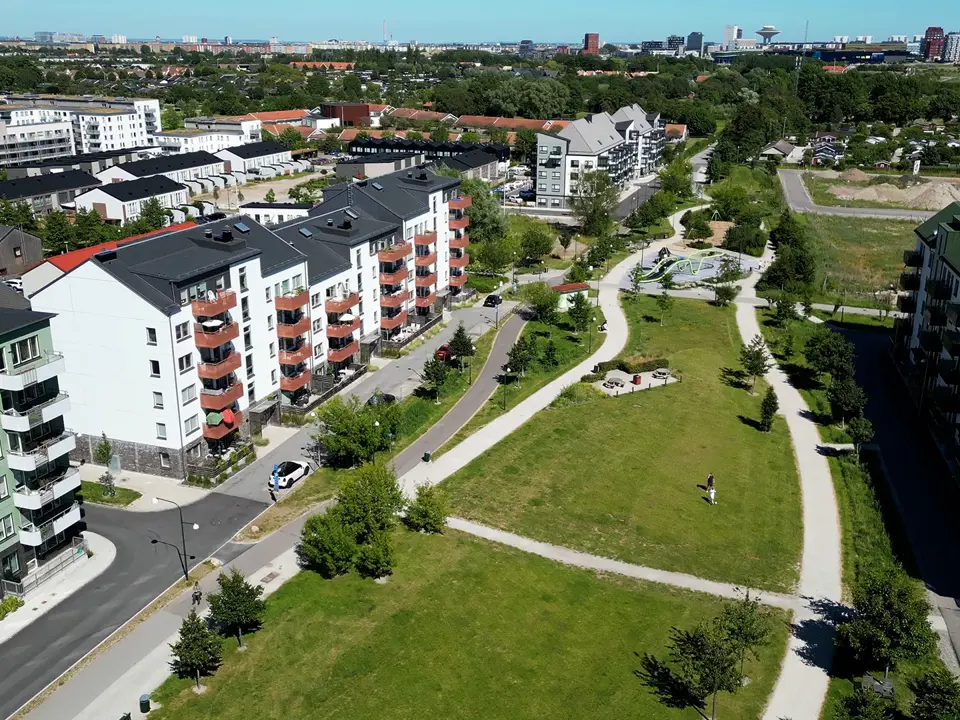 Flygbild över bostadsområde med flerbostadshus, park och gångvägar.