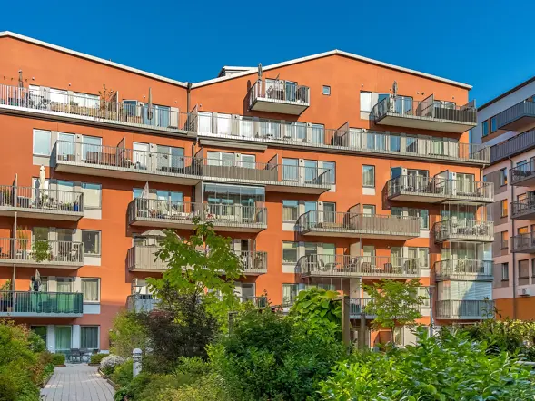 Grön innergård med röda fasader och balkonger i projekten Spinna och Väva i Hammarby Sjöstad.