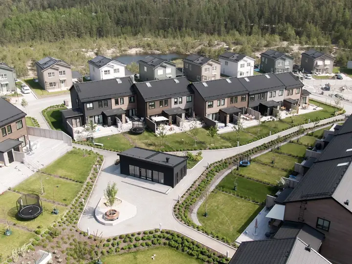 Flygbild över radhusområde med gångvägar, innergårdar och omgivande skog.
