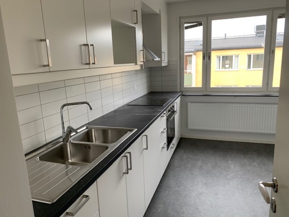 Ljust kök i en hyreslägenhet i Västerås med vita skåp, arbetsbänk och stort fönster.
