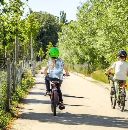 Två barn cyklar på en grönskande cykelväg.