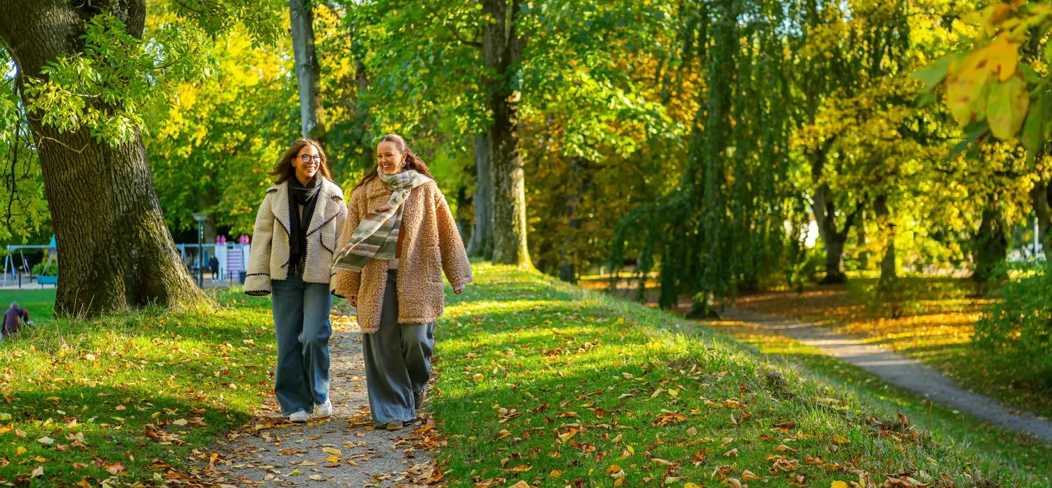 Två kvinnor promenerar genom en grön park i Lund.